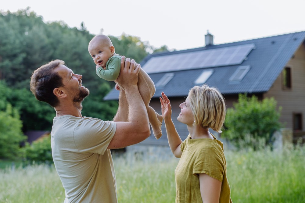 Famile på mor, far og baby foran hus med solceller på taget